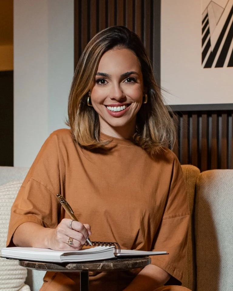 Mari Almeida sorrindo, escrevendo em um caderno espiral